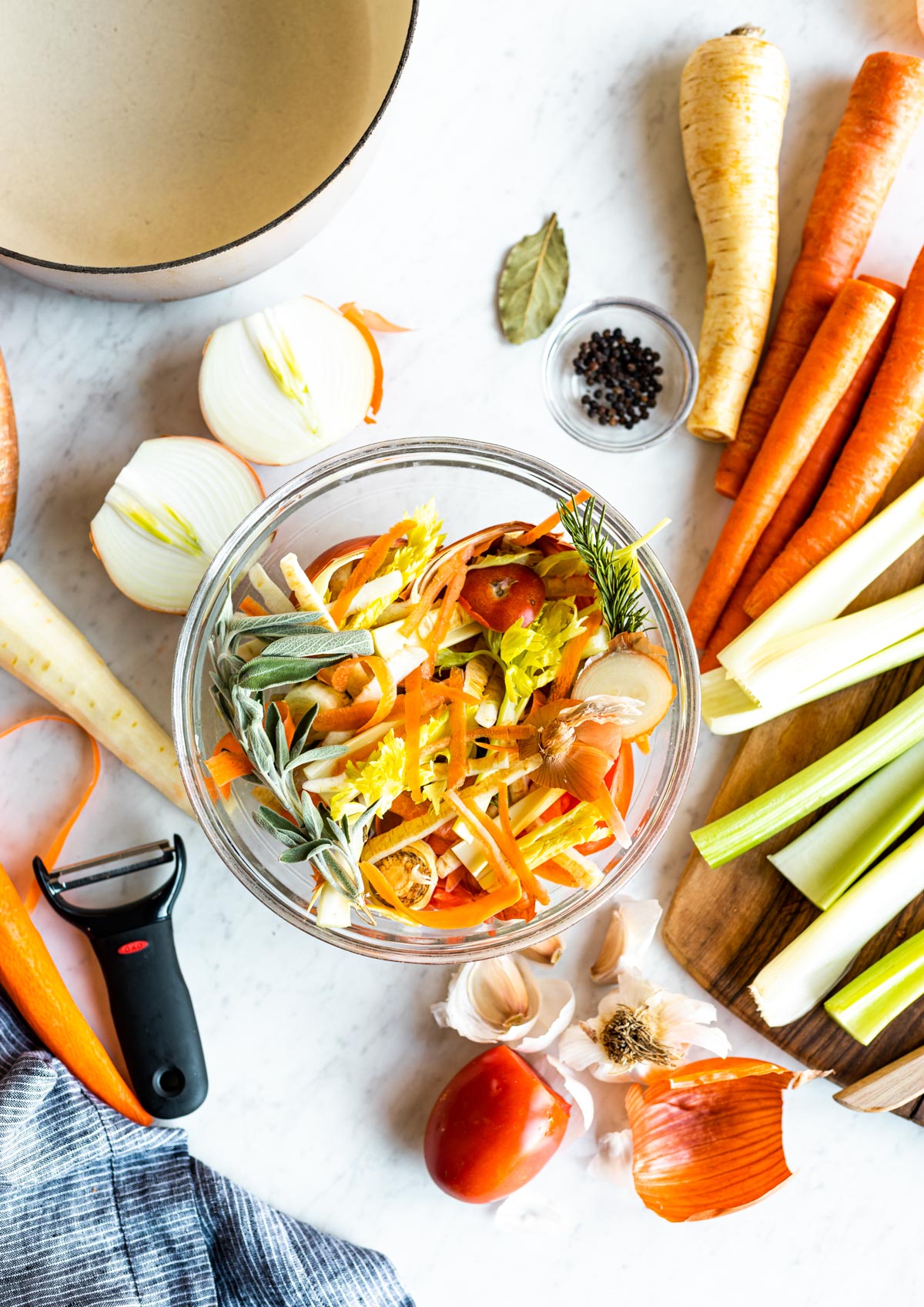 glass bowl of vegetable scraps surrounded by chopped vegetables.