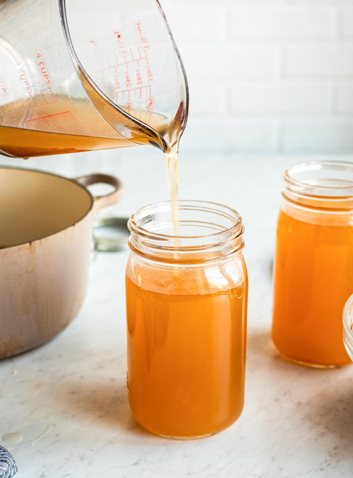 a glass measuring cup pouring vegetable stock into a glass mason jar.