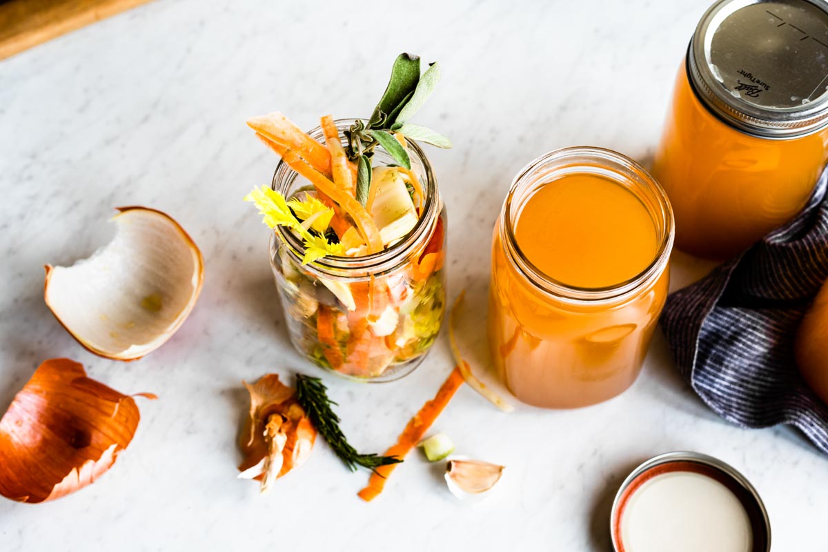 2 glass containers of homemade broth one with a lid and one without, and a 3rd glass container of veggie scraps.