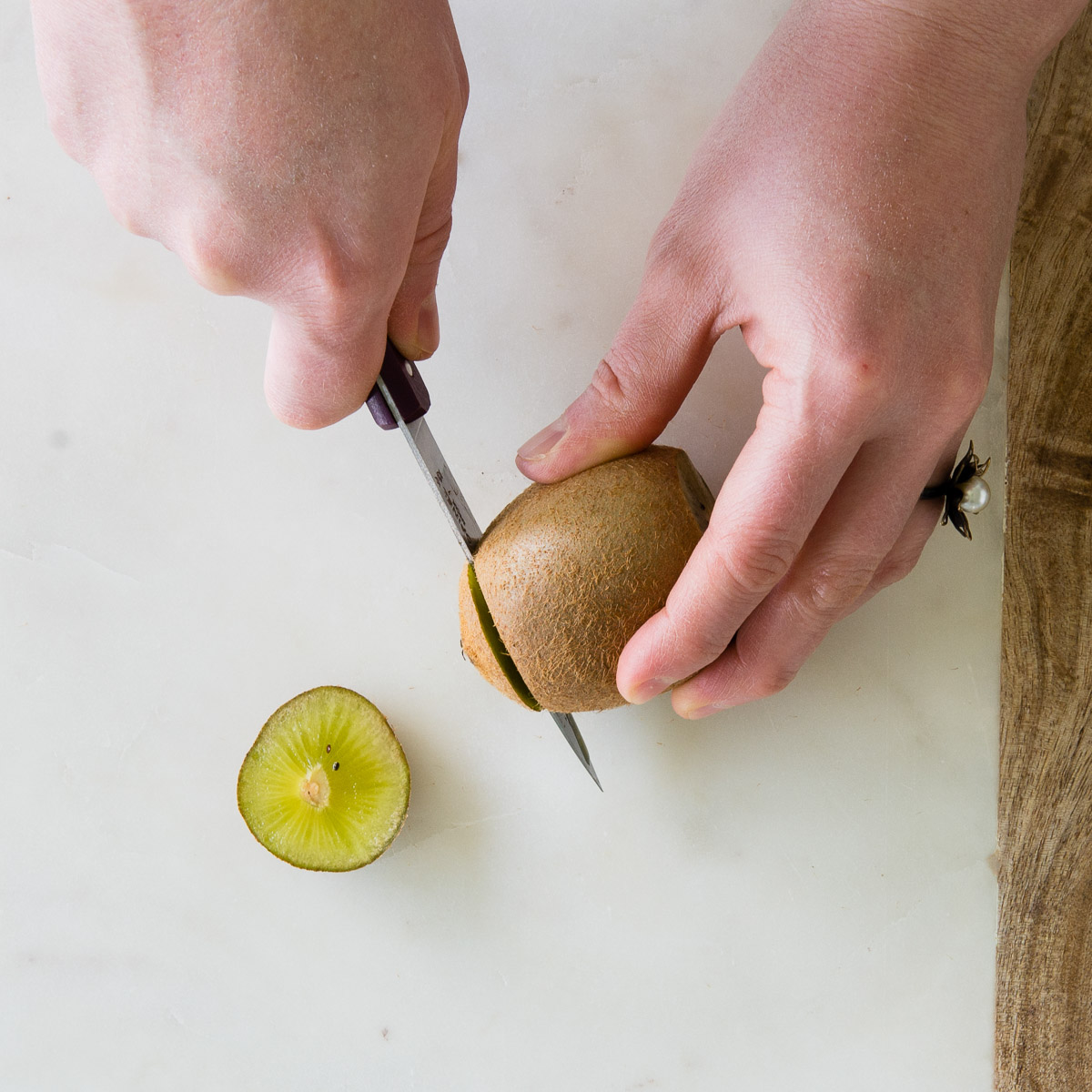 2 hands using a paring knife to cut the ends of a kiwi.