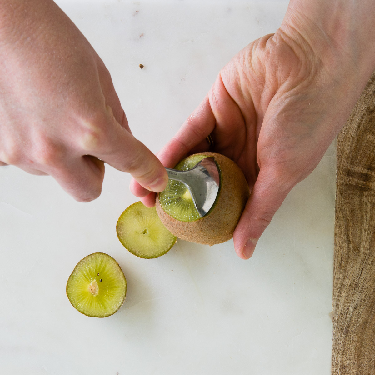 A person uses a spoon to peel the skin off a fresh kiwi