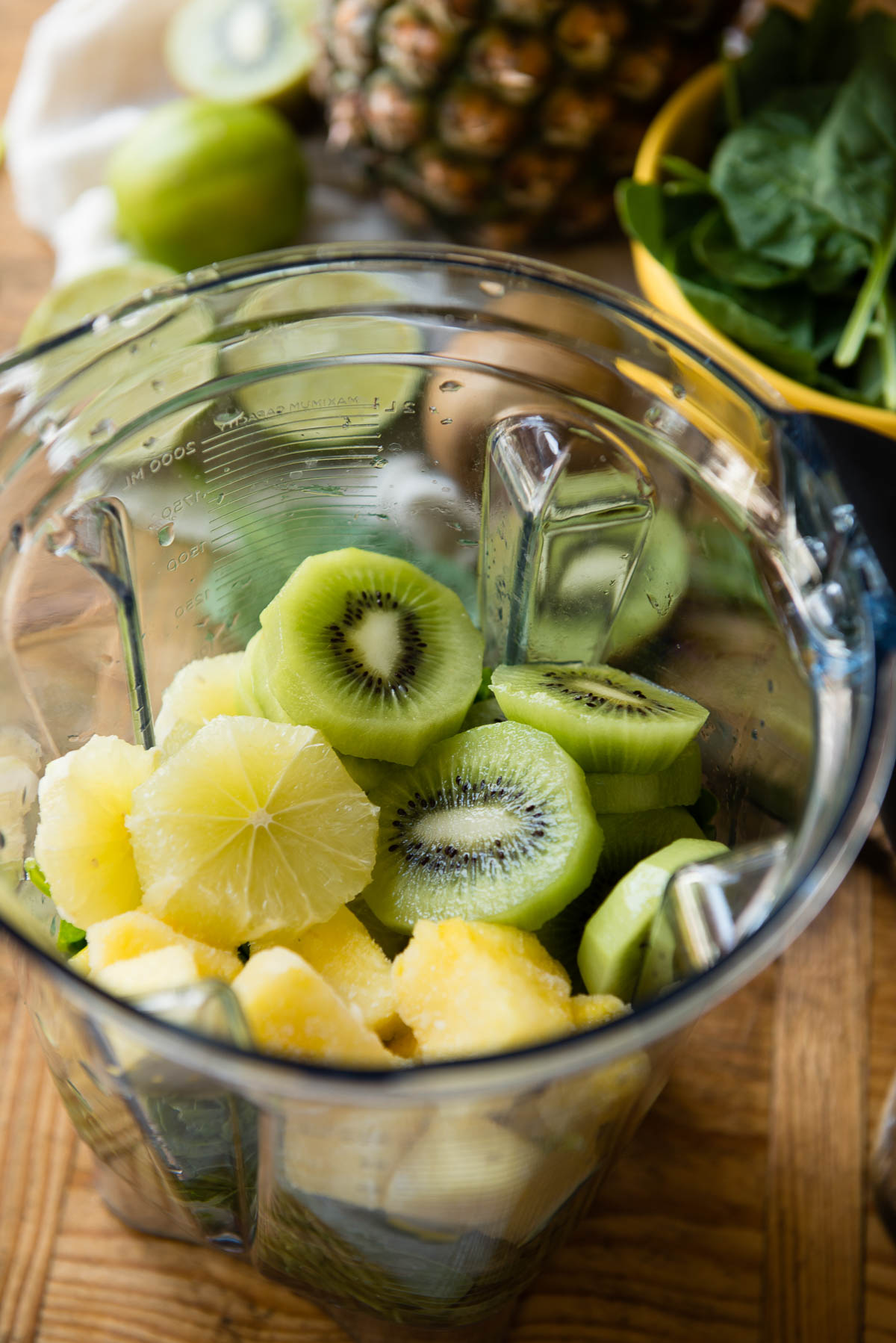 Vitamix blender container with sliced lemon, kiwi and frozen mango in it.