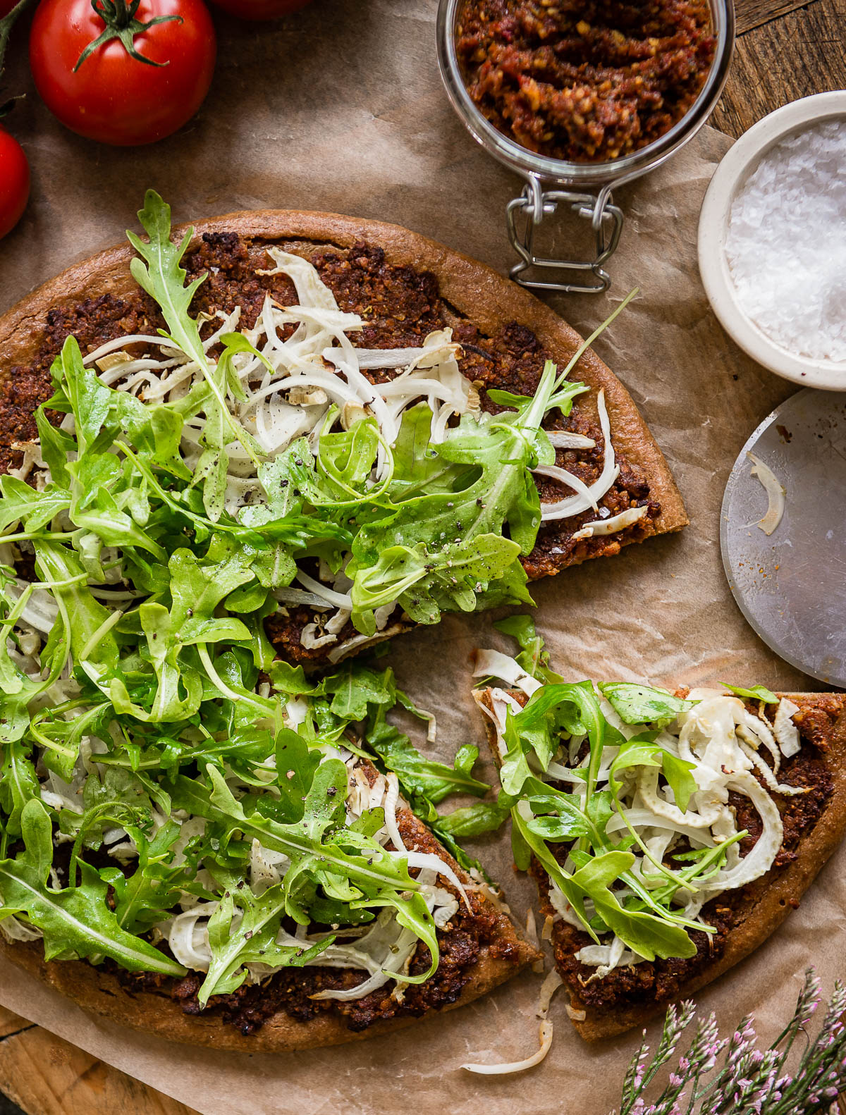 gluten free pizza sliced and topped with fennel and arugula on a parchment paper.