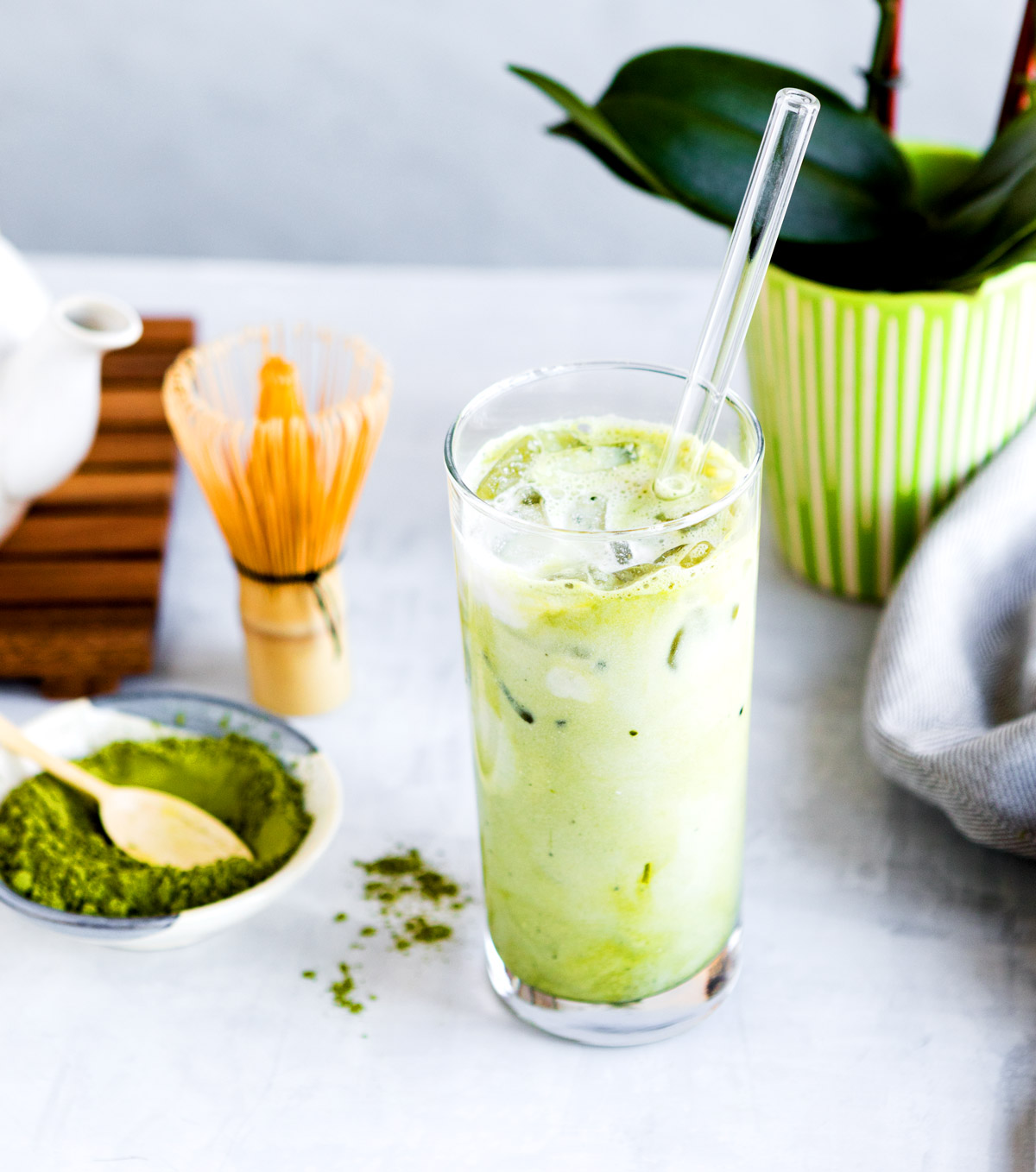 vanilla matcha latte in a glass with ice and bowl of matcha powder on table.