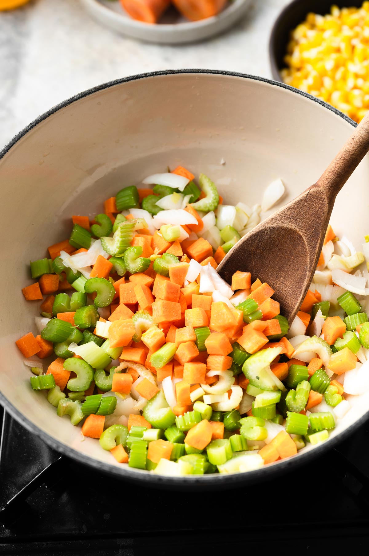 Up close view of chopped carrots, onions and celery in a pot with a wood spoon.