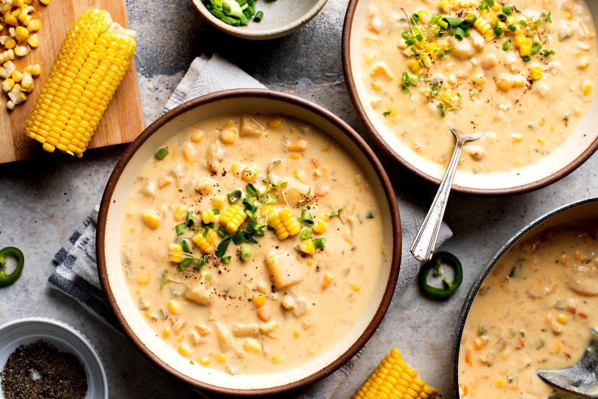 A table setting with bowls of vegan corn chowder and fresh corn on the cob.