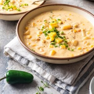 White bowl of vegan corn chowder and jalapeno pepper on the side.