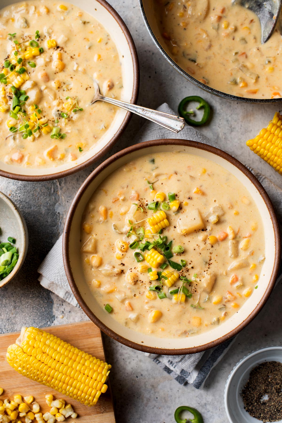 Off white pottery bowl with vegan corn chowder soup and slices of jalapenos on the gray countertop.