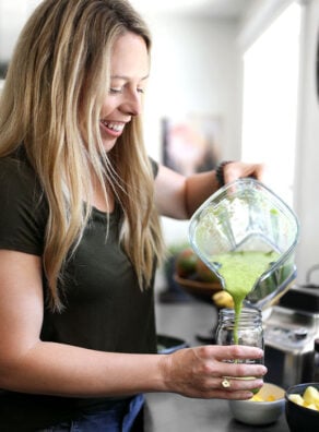 Jen smiling while pouring a green smoothie from a blender into a jar.