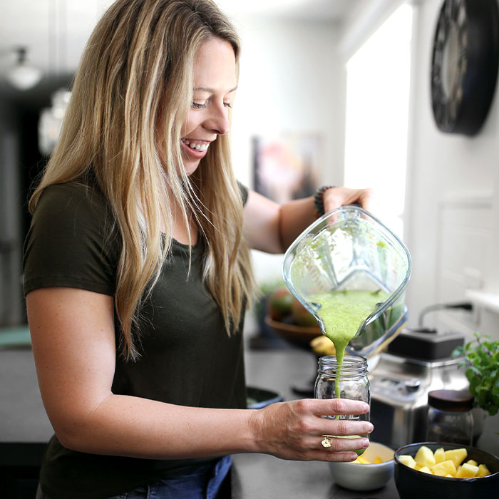 Jen smiling while pouring a green smoothie from a blender into a jar.