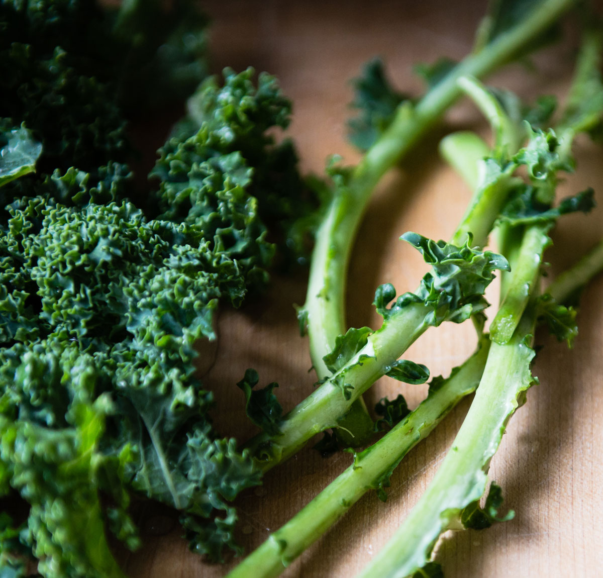 Removing kale leaves from stems on a butting board.