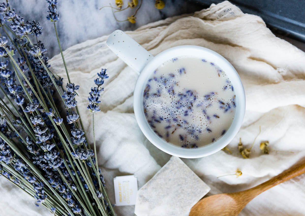 fresh herbal tea with flowers in a white mug on a tea towel with a bunch of fresh lavender next to it.