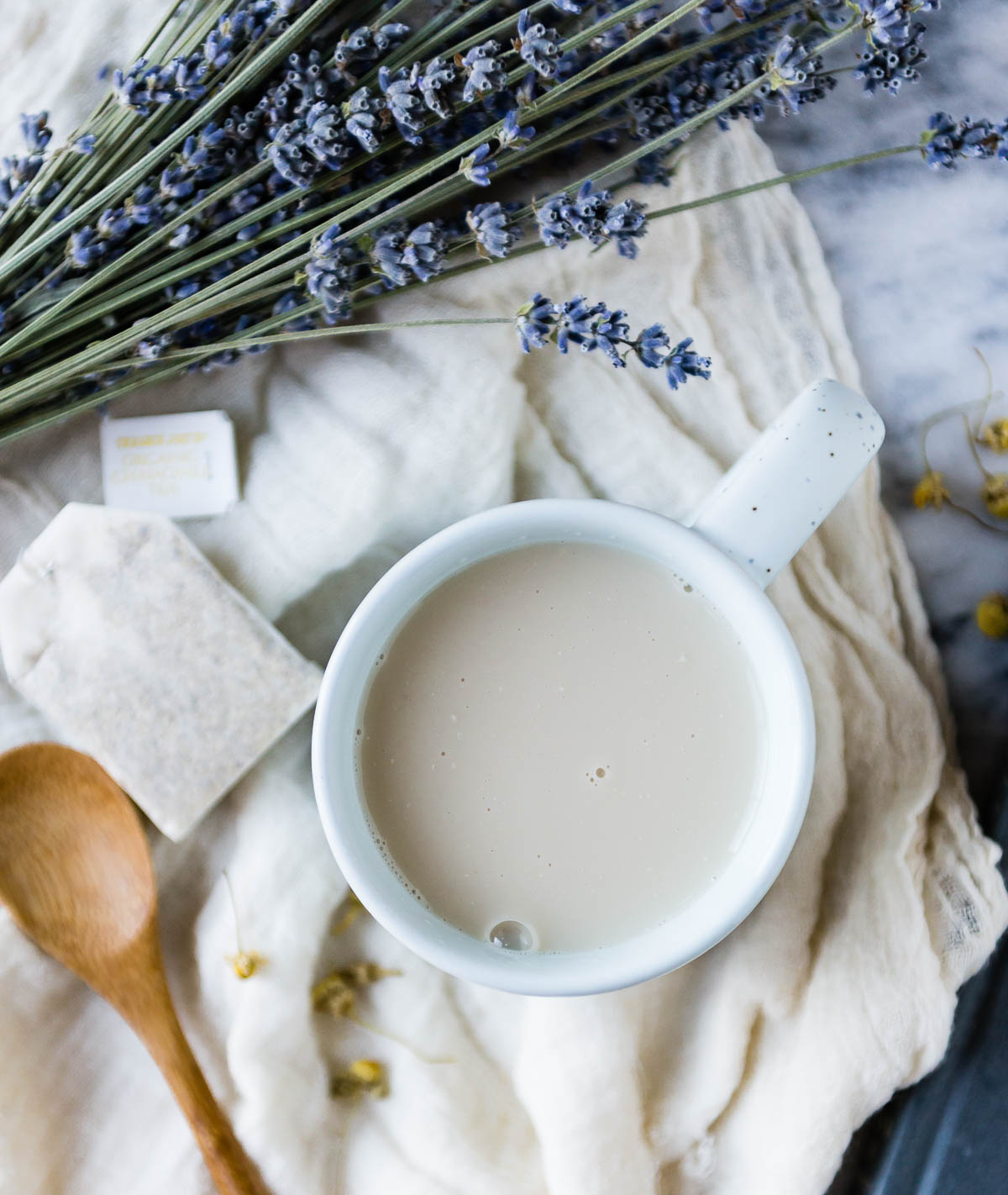 herbal tea in a white mug on a tea towel next to an unused tea bag, wooden spoon and fresh lavender.