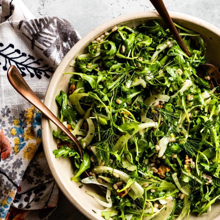 arugula salad. in a bowl with salad tongs.