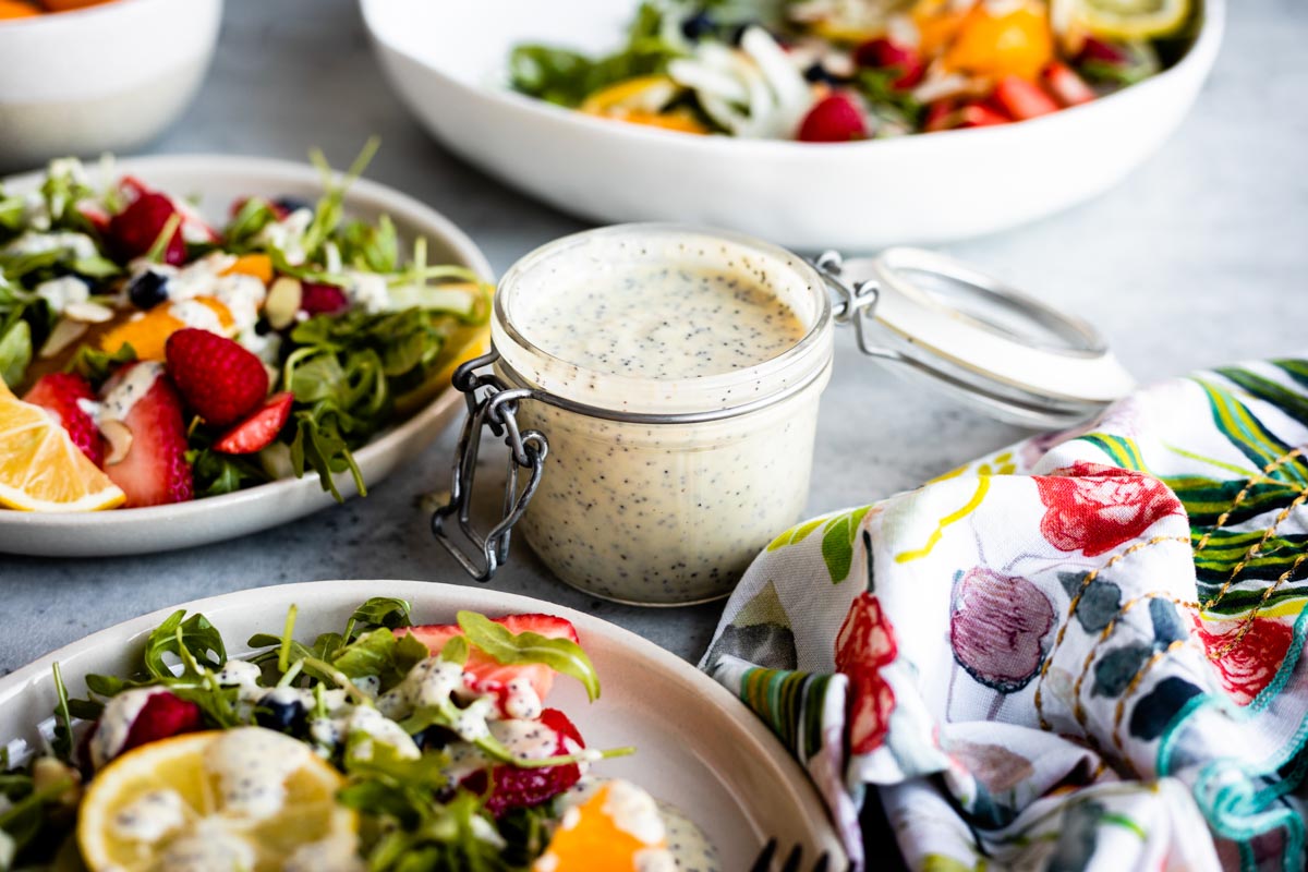 lemon vinaigrette in a glass jar next to white plates full of salad with berries.