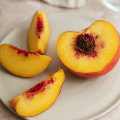 Close-up of a ripe peach, pit, and slices on a white plate, emphasizing fresh, juicy, healthy qualities.