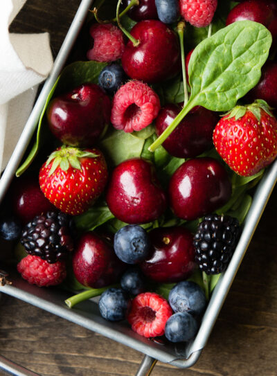 Top view of a metal tray overflowing with fresh berries, including strawberries, blackberries, raspberries, cherries, and blueberries.