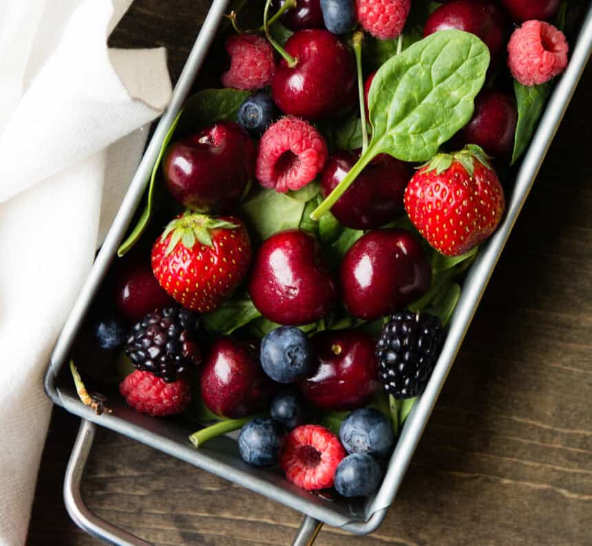 Top view of a metal tray overflowing with fresh berries, including strawberries, blackberries, raspberries, cherries, and blueberries.