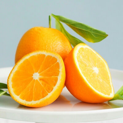 Two oranges on a white plate, one sliced in half.