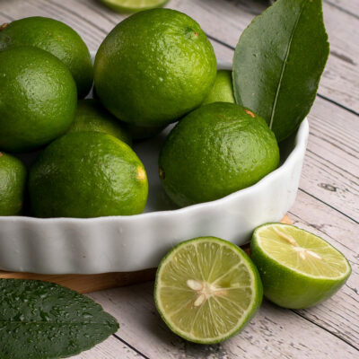 Shallow bowl of vibrant green limes with one halved lime beside it.