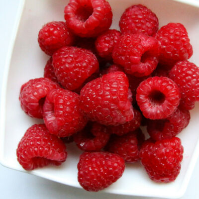A small, white dish brimming with fresh raspberries.