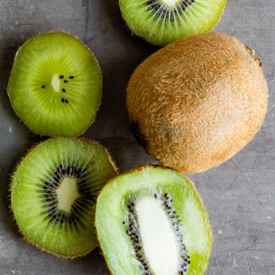 Top-down view of a whole kiwi surrounded by sliced kiwi on a gray counter.