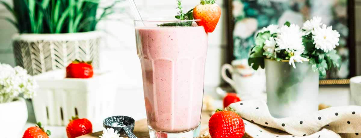 a pink smoothie with a strawberry on the rim of the glass and other strawberries sitting on the table with multiple flowers