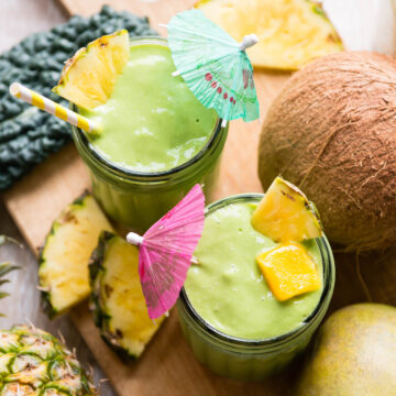 mango kale smoothie in glasses with tropical umbrellas