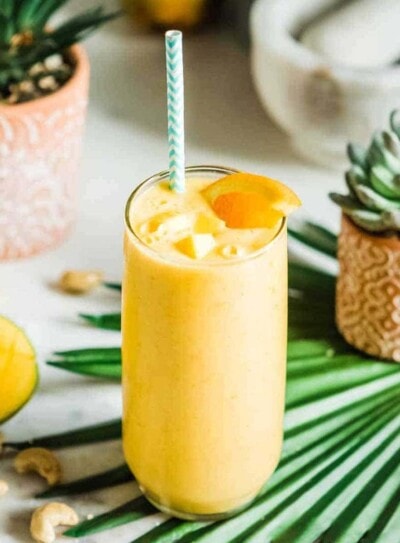 mango smoothie in a tall glass with a paper straw.