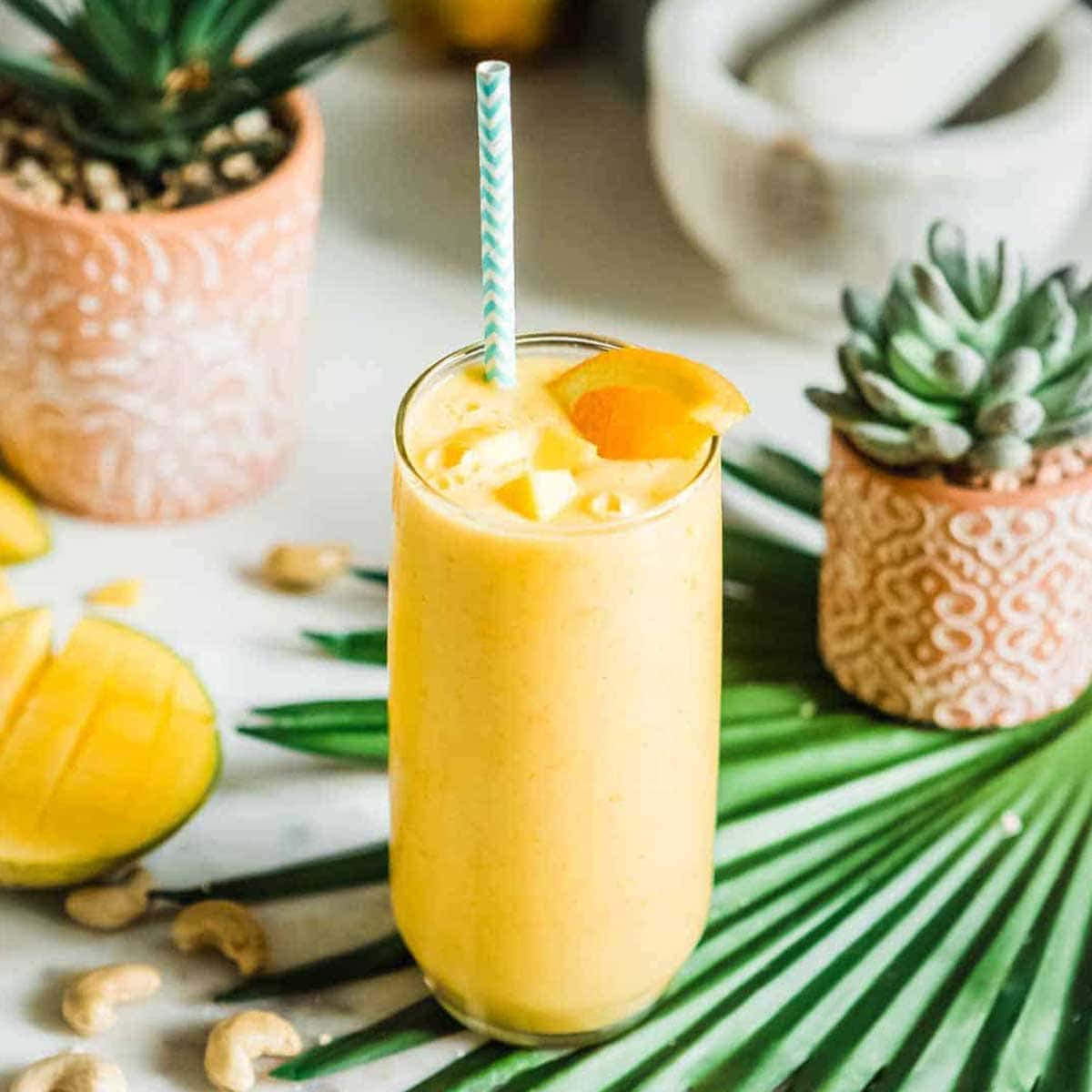 mango smoothie topped with mango chunks and orange garnish in glass cup with green straw.