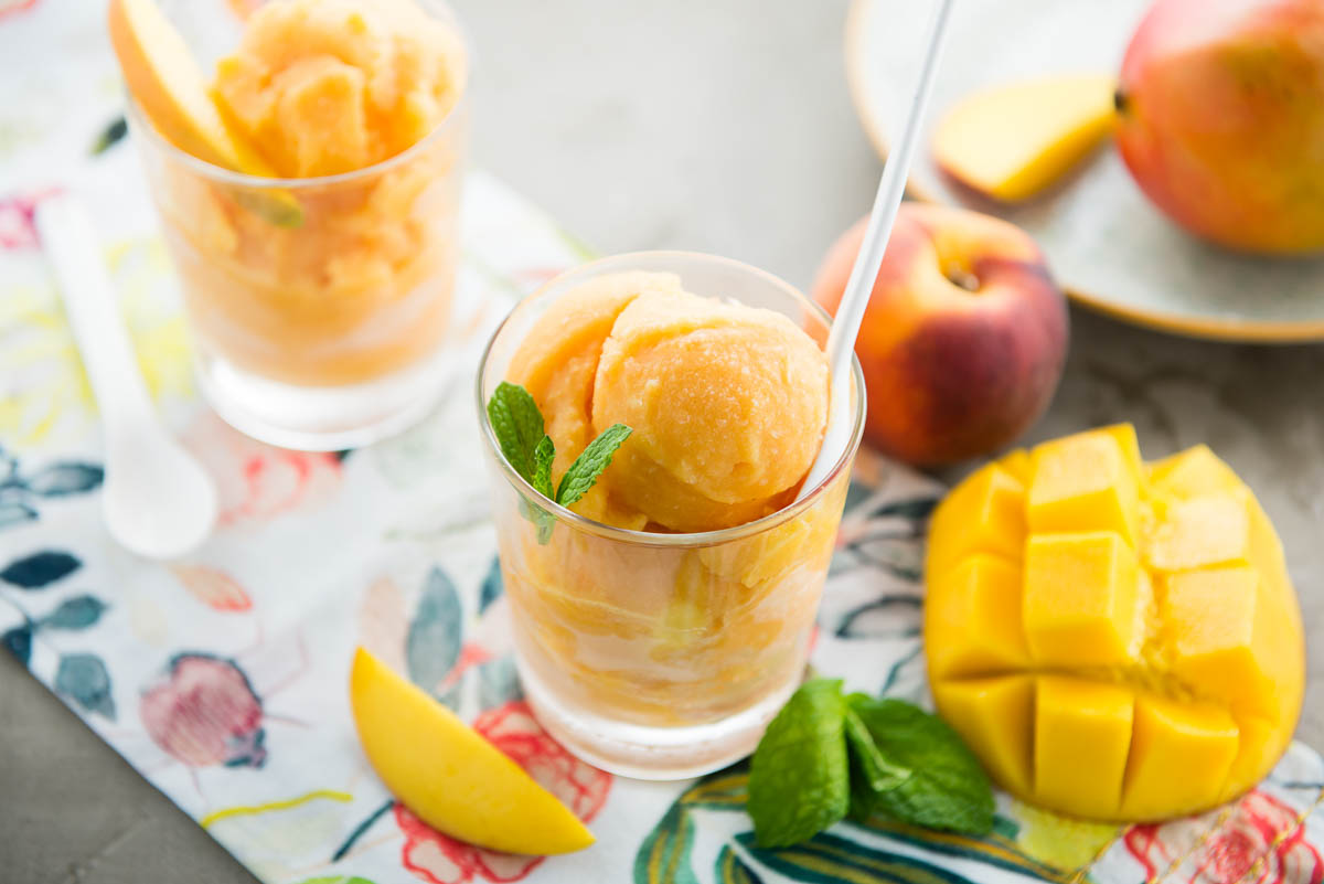 glass of orange colored dessert with white spoon on a colorful tea towel.