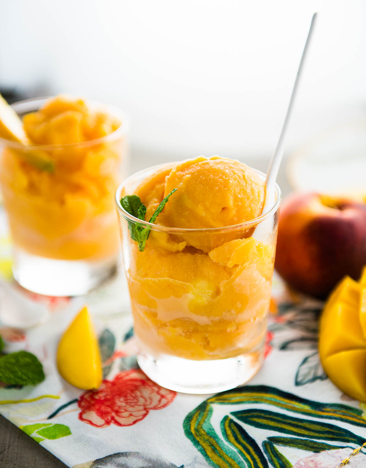 peach mango sorbet in a glass with fresh mint and a white spoon.