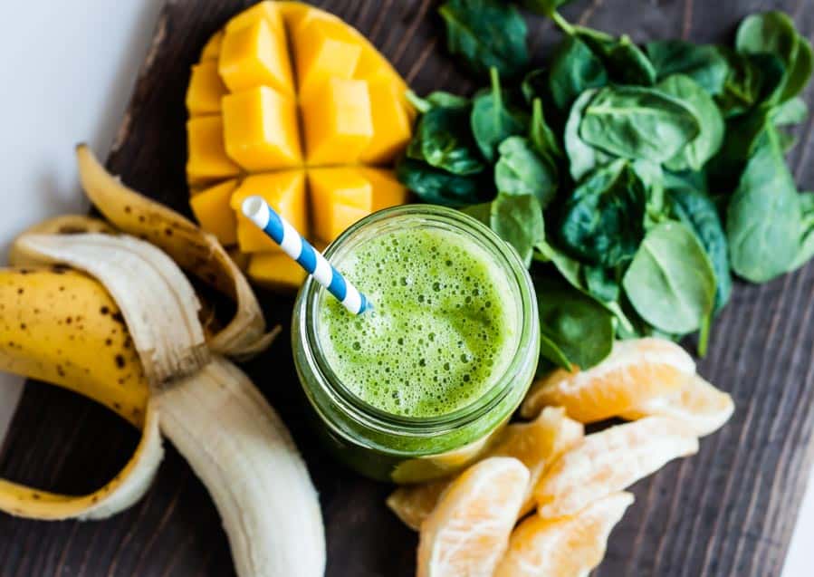 mango spinach smoothie in glass jar with blue and white striped paper straw.