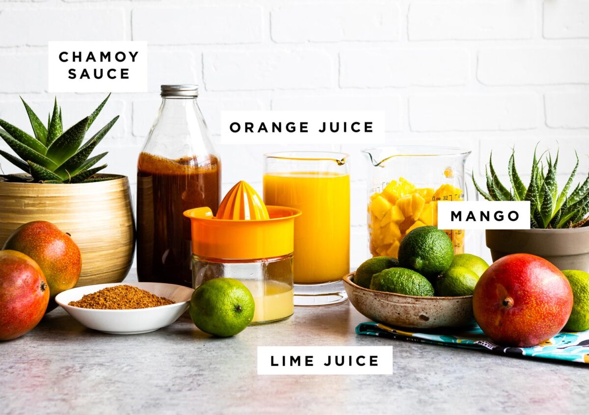 mangonada ingredients on countertop including chamoy sauce, orange juice, mango and lime juice.