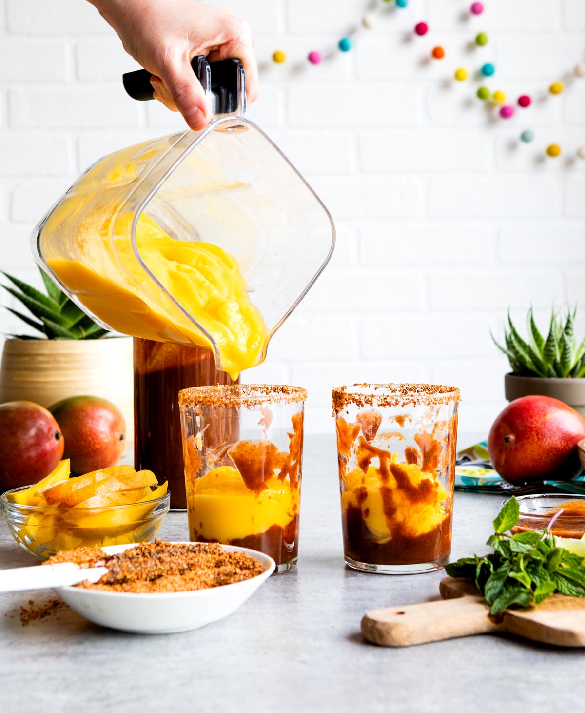 pouring creamy mangonada into glasses with chamoy and diced mango on top.