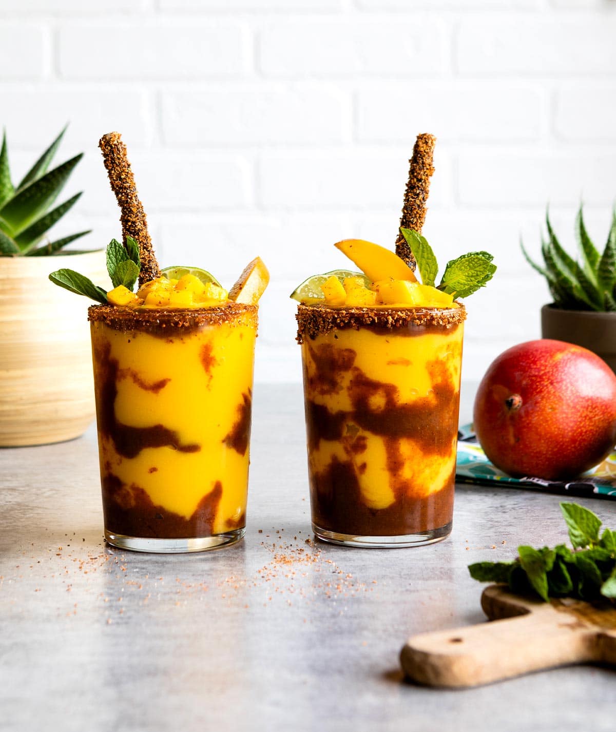 2 glasses of mangonada topped with fresh fruit and a tamarind straw.