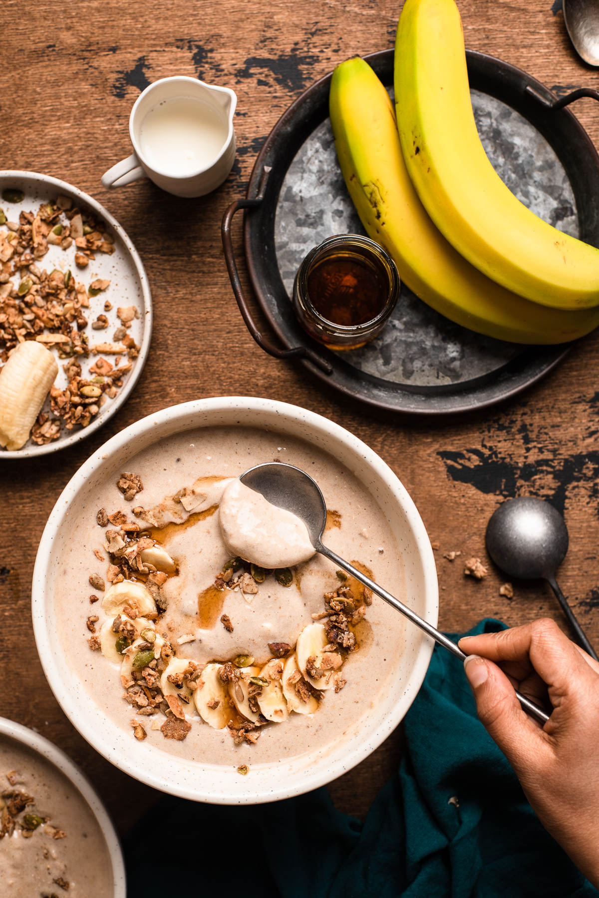 long silver spoon scooping out a maple smoothie bowl topped with granola, maple syrup and banana slices on a wooden table.