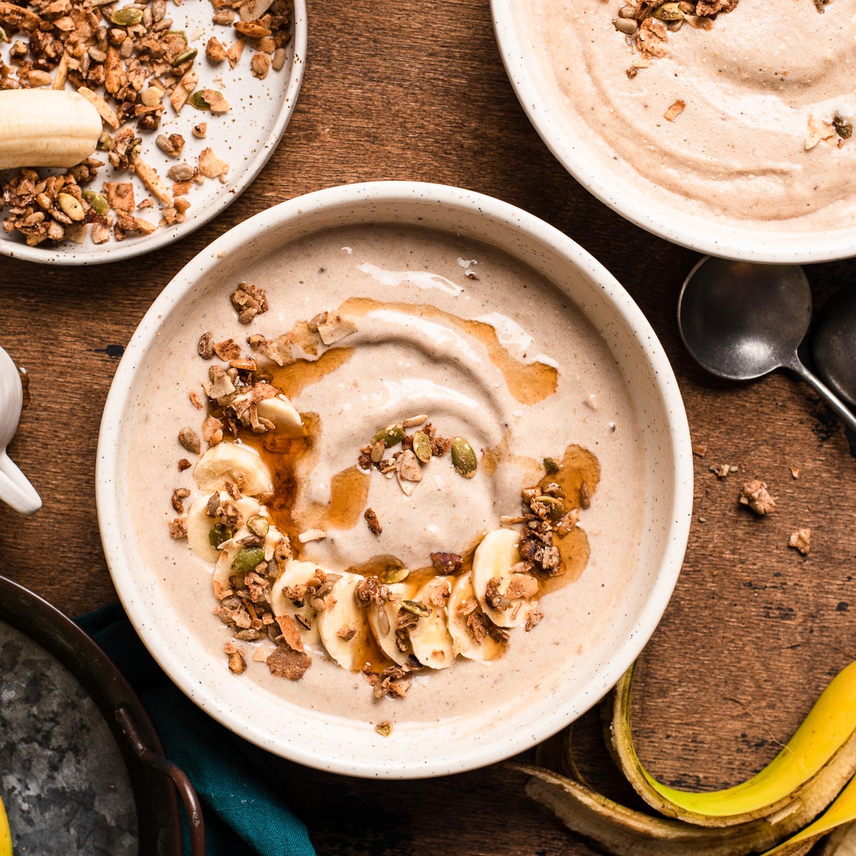 2 oat smoothie bowls topped with maple syrup and granola, next to a bowl of granola and banana.