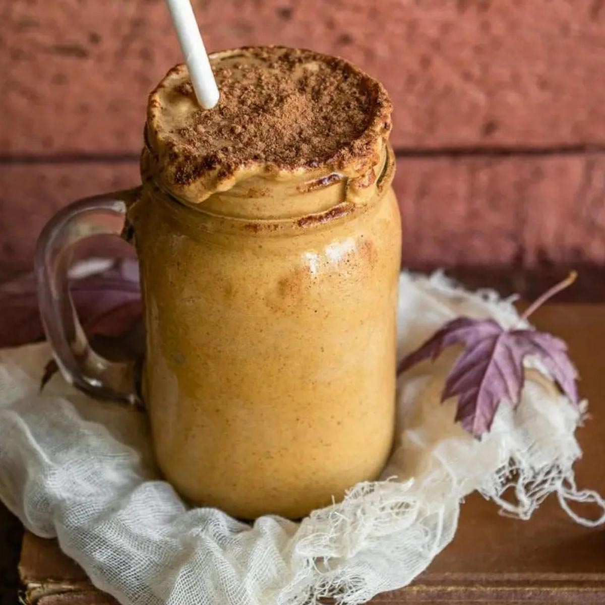 Maple pumpkin smoothie in a handled jar with a straw.