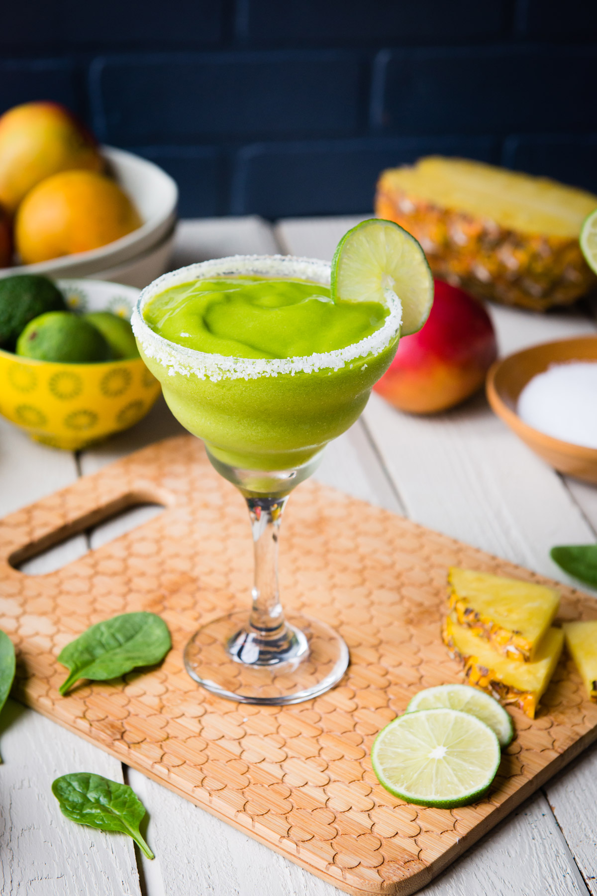 Beautiful margarita glass full of smoothie on table with fresh cut limes and pineapple.