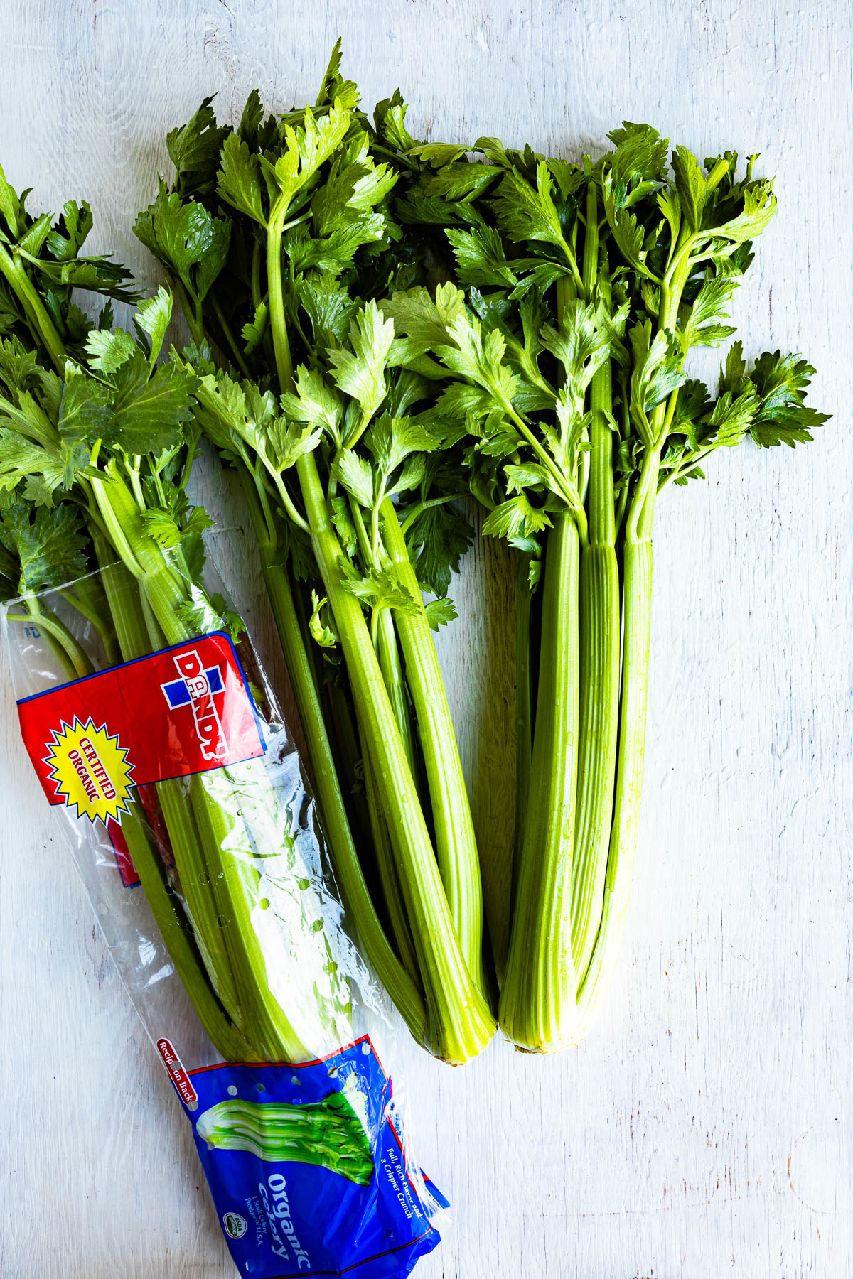 3 heads of celery with leaves, one in a bag with the words Dandy on it.