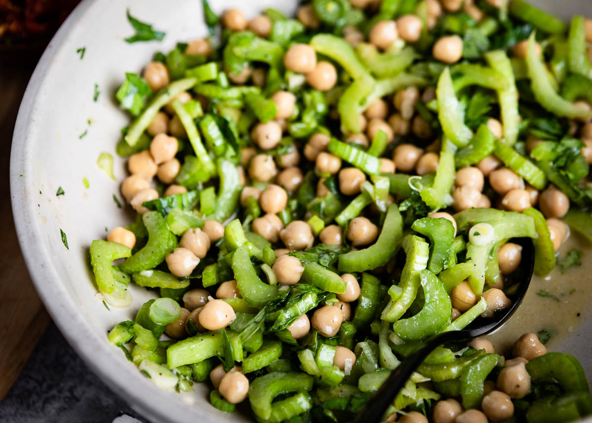 mixing together ingredients for salad recipe in white bowl.