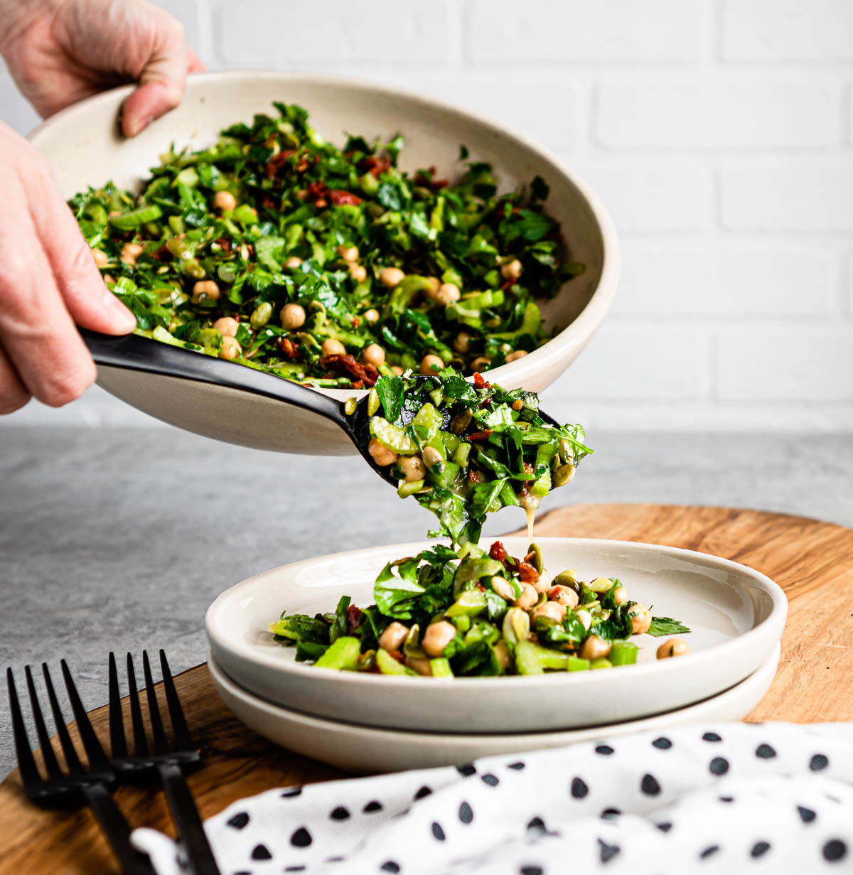 scooping marinated celery salad out of a bowl and onto a plate using a big black spoon.