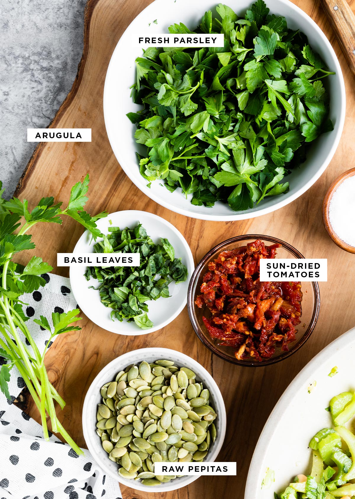 labeled serving ingredients including arugula, fresh parsley, basil leaves, sun-dried tomatoes and raw pepitas.