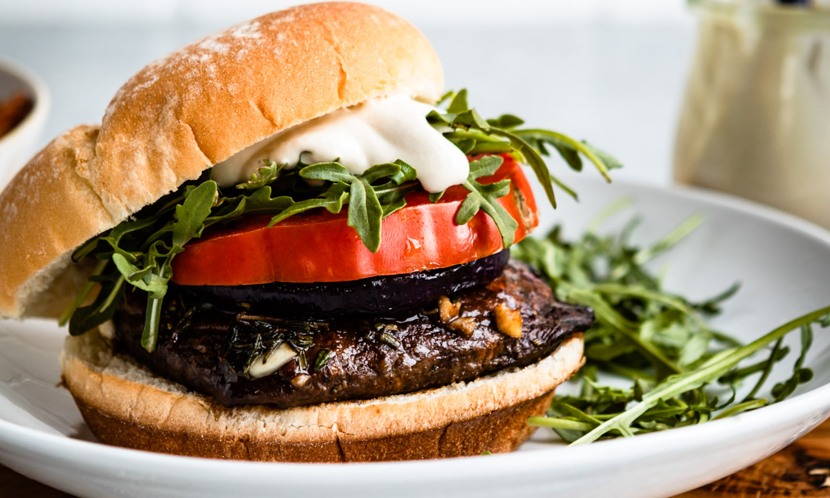 portobello mushroom burger on a bun with tomato, garlic aioli and arugula. 