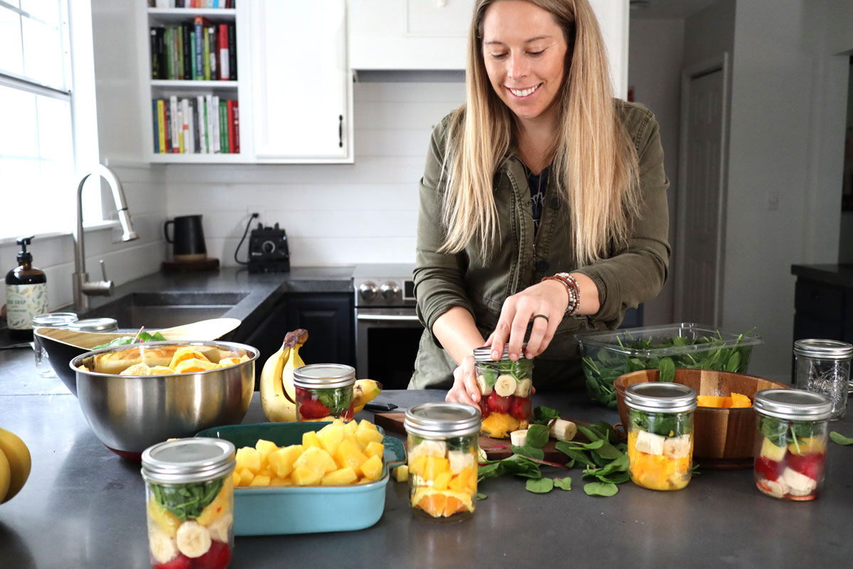 Woman in kitchen prepping smoothies in mason jars to put in freezer.