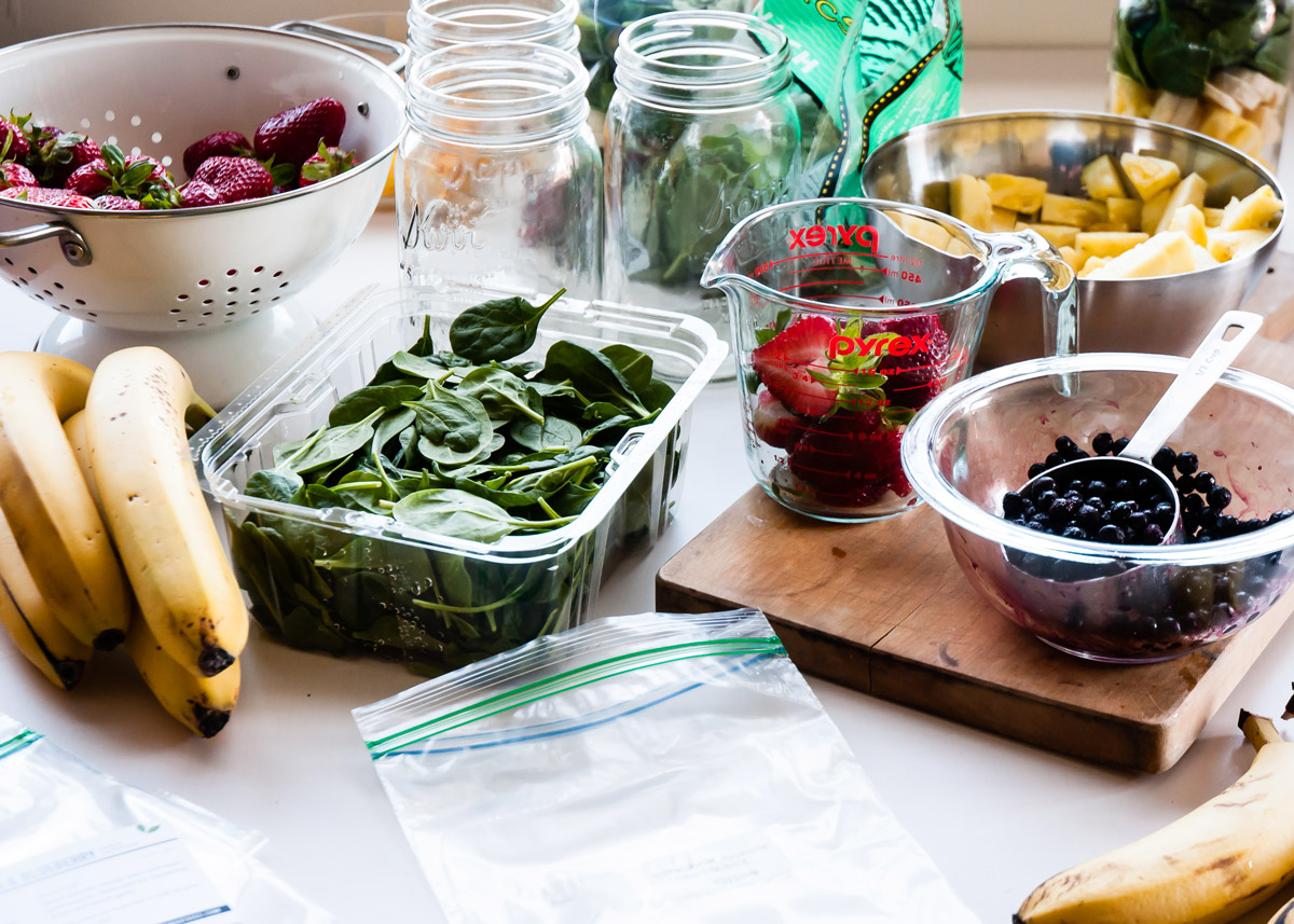 Fresh spinach, strawberries and bananas on kitchen counter with measuring cup to make smoothie packs.