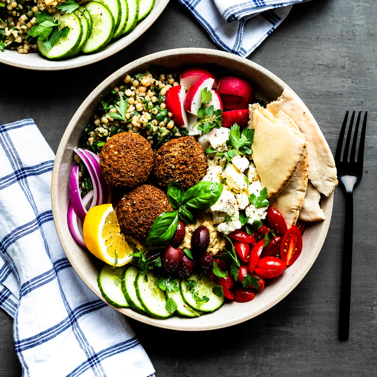 Mediterranean falafel bowl with fresh ingredients in a ceramic bowl on a concrete counter top.