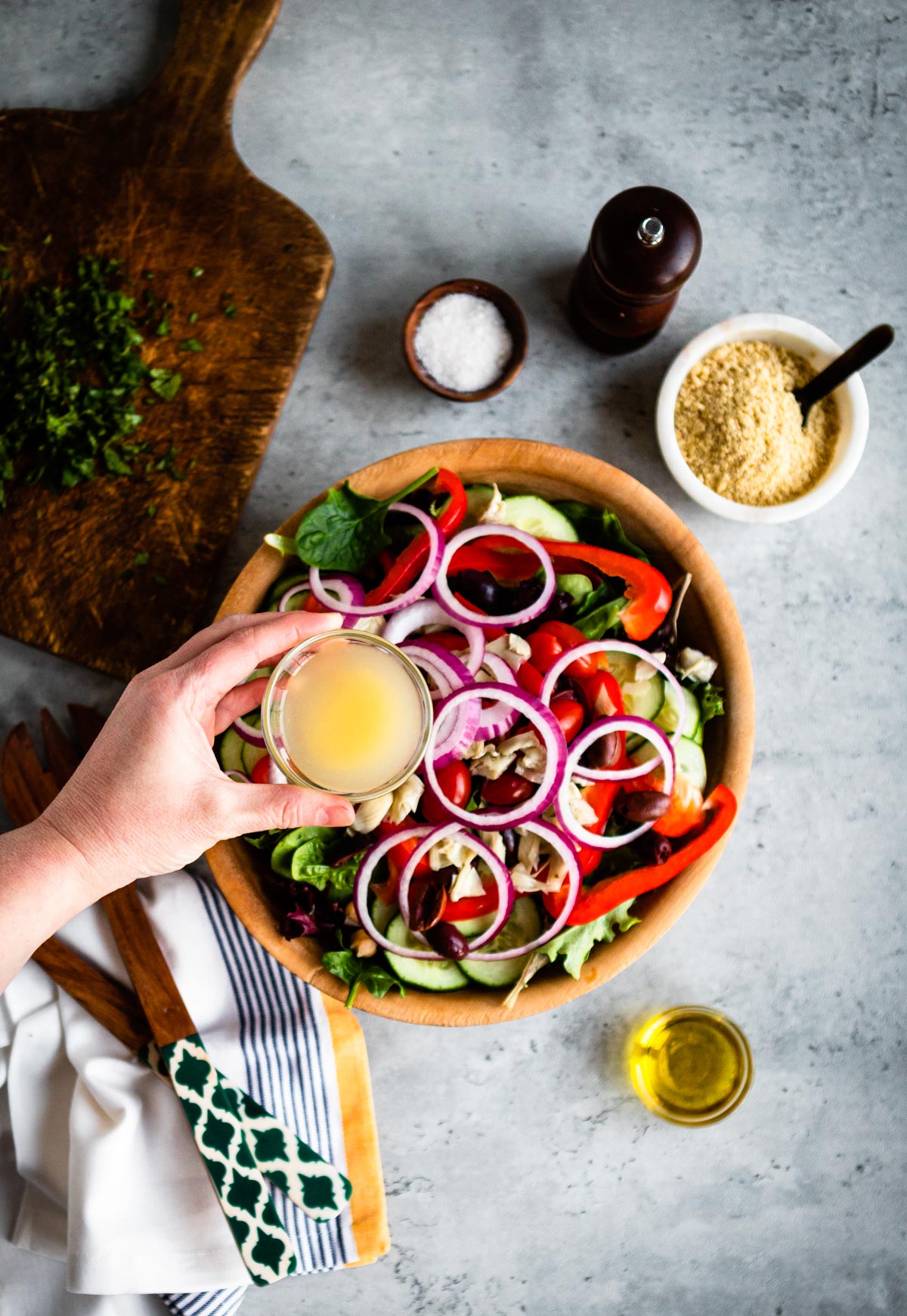 simple dressing in a glass bowl ready to pour over greek salad in wooden bowl.