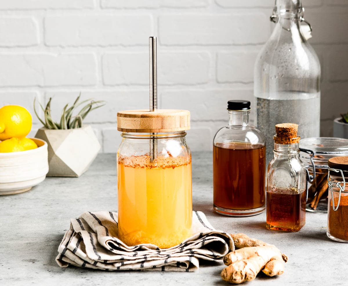 glass jar of metabolism boosting tea with wooden lid and stainless steel straw next to glass jars of apple cider vinegar, honey and cayenne.